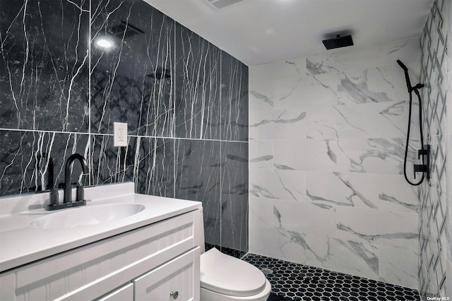 bathroom featuring tiled shower, vanity, toilet, and tile walls