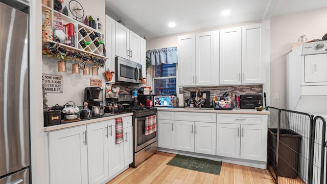 2350 Waterbury Ave, Bronx, NY 10462 - kitchen featuring appliances with stainless steel finishes, decorative backsplash, light wood-style flooring, white cabinetry, and stacked washer and clothes dryer