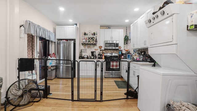 kitchen with white cabinetry, stacked washer and dryer, stainless steel appliances, and light hardwood / wood-style floors