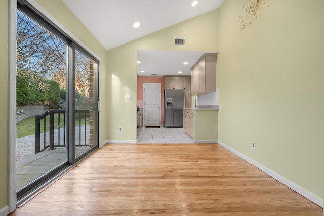 interior space featuring stainless steel refrigerator with ice dispenser, light hardwood / wood-style floors, and high vaulted ceiling