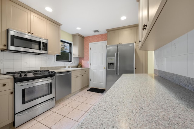 kitchen with light tile patterned floors, cream cabinetry, appliances with stainless steel finishes, decorative backsplash, and sink