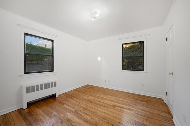 spare room featuring radiator, ornamental molding, and light wood-type flooring