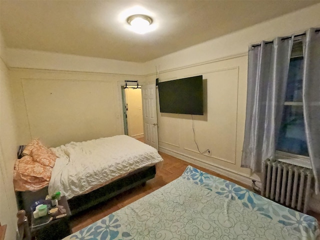 bedroom featuring dark hardwood / wood-style flooring, a barn door, and radiator