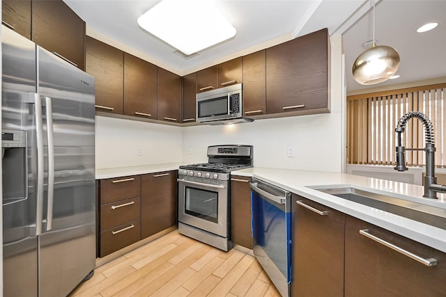 kitchen featuring dark brown cabinetry, stainless steel appliances, sink, decorative light fixtures, and light hardwood / wood-style flooring