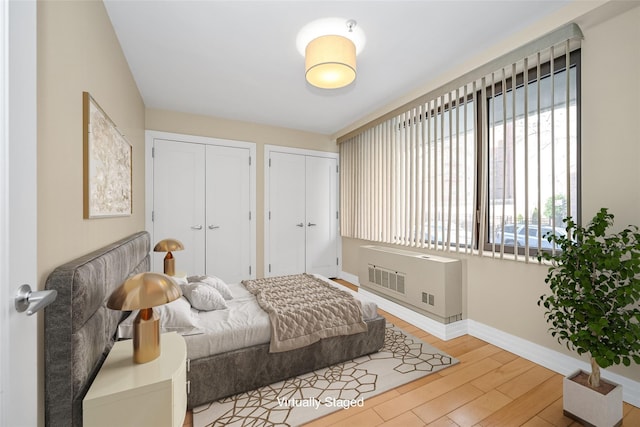 bedroom with two closets and light hardwood / wood-style flooring