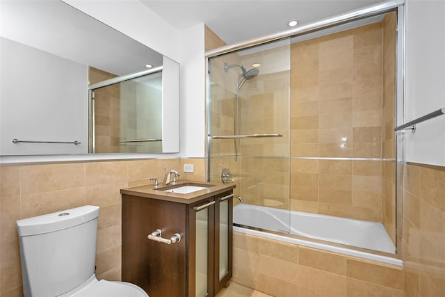 full bathroom featuring combined bath / shower with glass door, vanity, toilet, and tile walls