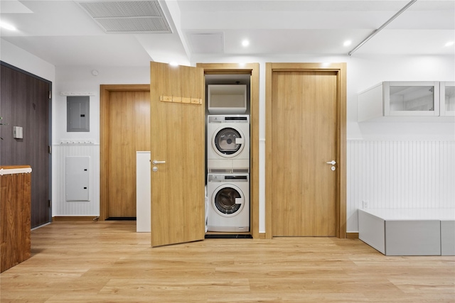 laundry area featuring electric panel, light hardwood / wood-style flooring, and stacked washer / drying machine