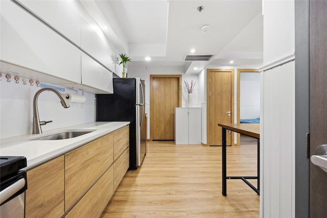 kitchen with stainless steel refrigerator, white cabinetry, sink, light hardwood / wood-style flooring, and stove