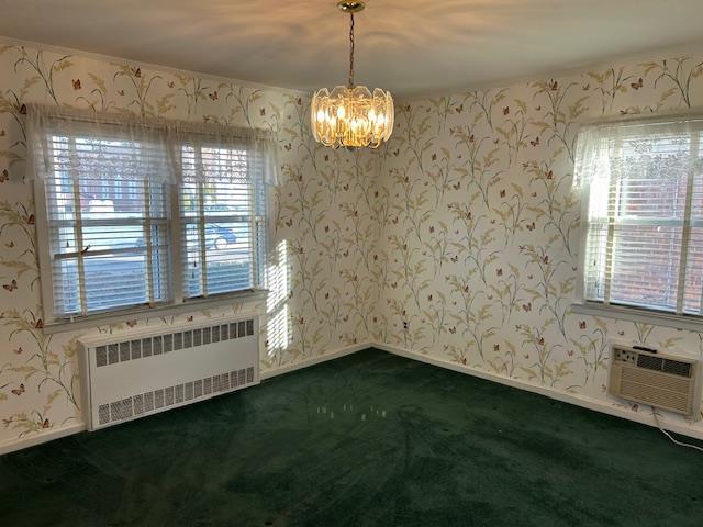 carpeted spare room featuring an AC wall unit, radiator heating unit, and a notable chandelier