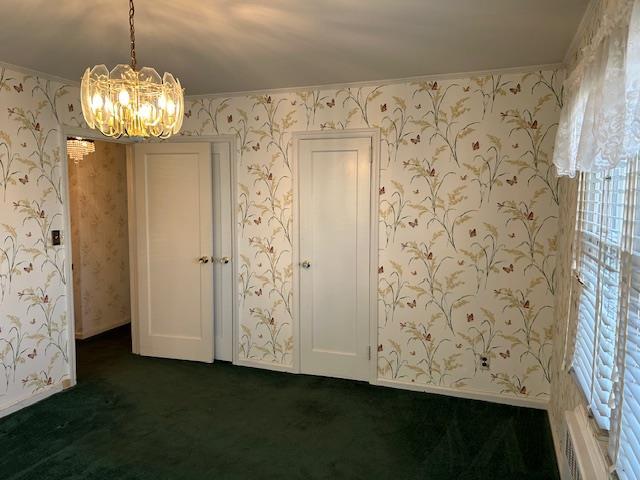 empty room with dark colored carpet, ornamental molding, and a notable chandelier