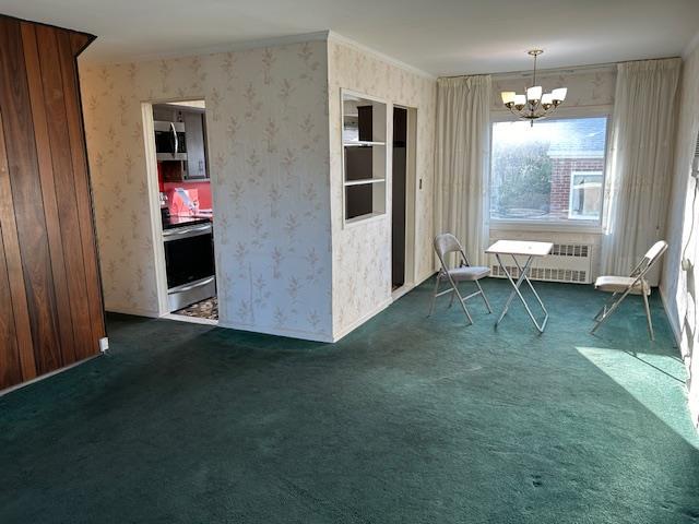 spare room featuring dark carpet, radiator, and a notable chandelier