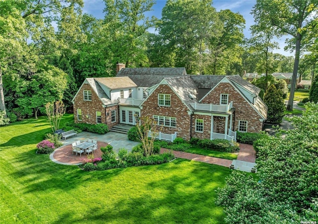 tudor-style house featuring a patio area, french doors, a balcony, and a front yard