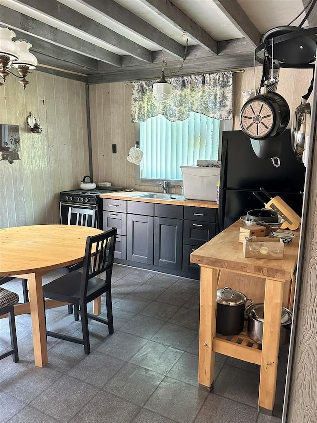 kitchen featuring black fridge, sink, wooden walls, beamed ceiling, and range with gas stovetop