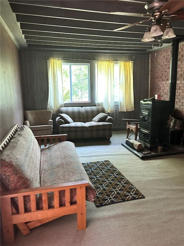 sitting room with carpet flooring, a wood stove, ceiling fan, and brick wall