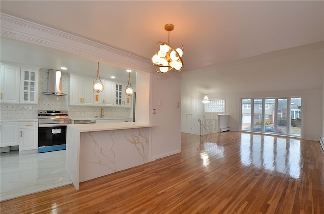 kitchen featuring white cabinets, appliances with stainless steel finishes, wall chimney range hood, and a notable chandelier