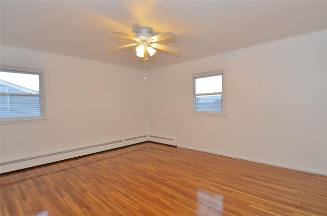 spare room with ceiling fan, a wealth of natural light, a baseboard heating unit, and light wood-type flooring