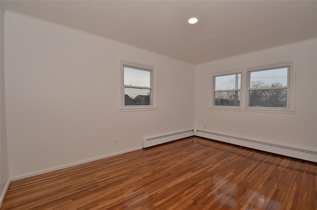 spare room featuring a baseboard heating unit and hardwood / wood-style flooring