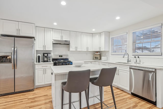 kitchen with sink, light hardwood / wood-style flooring, appliances with stainless steel finishes, white cabinetry, and a center island