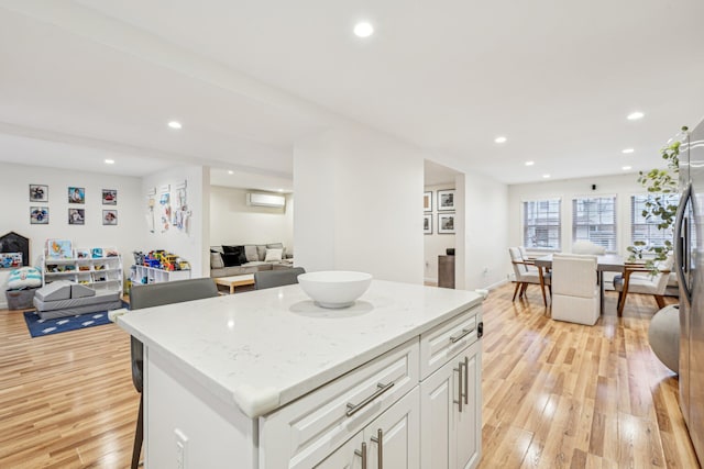 kitchen with a wall mounted air conditioner, white cabinetry, a center island, light stone counters, and light hardwood / wood-style floors