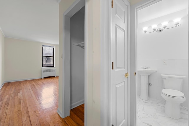 bathroom featuring sink, wood-type flooring, tile walls, radiator heating unit, and toilet