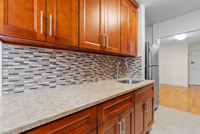 kitchen with light stone countertops, sink, stainless steel fridge, decorative backsplash, and light tile patterned flooring