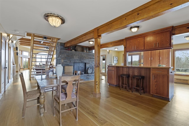 dining space with beam ceiling, a stone fireplace, and light hardwood / wood-style flooring