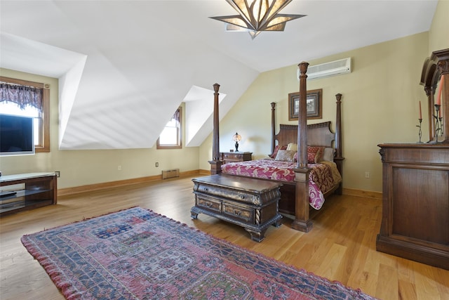 bedroom with a wall mounted air conditioner, light hardwood / wood-style floors, and vaulted ceiling