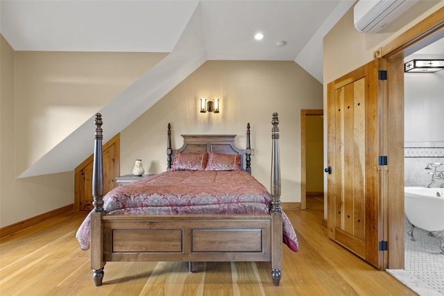 bedroom featuring a wall mounted AC, vaulted ceiling, and light hardwood / wood-style flooring