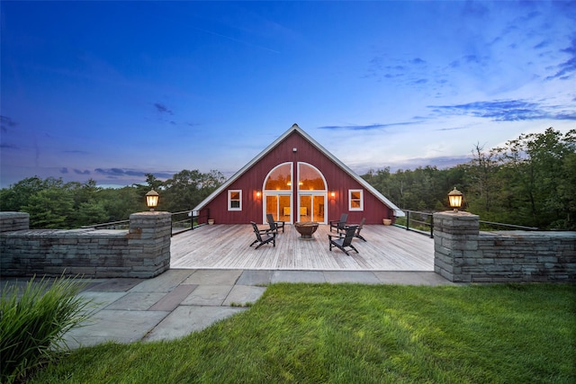 back house at dusk with a wooden deck, a yard, and a fire pit