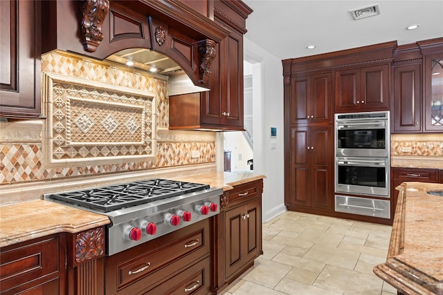 kitchen with decorative backsplash, appliances with stainless steel finishes, light stone countertops, and custom exhaust hood