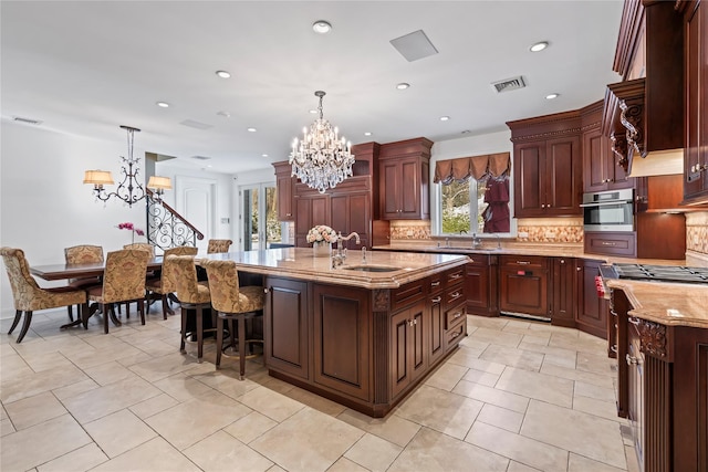 kitchen with hanging light fixtures, a center island with sink, a notable chandelier, oven, and decorative backsplash