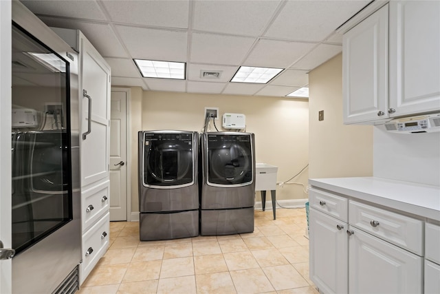 clothes washing area with cabinets, light tile patterned floors, and washer and clothes dryer