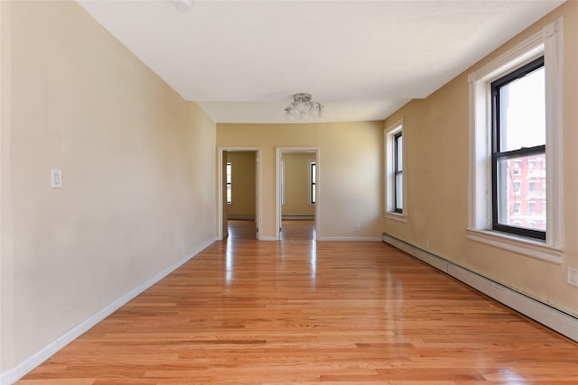 empty room with a healthy amount of sunlight, light hardwood / wood-style floors, and a baseboard heating unit