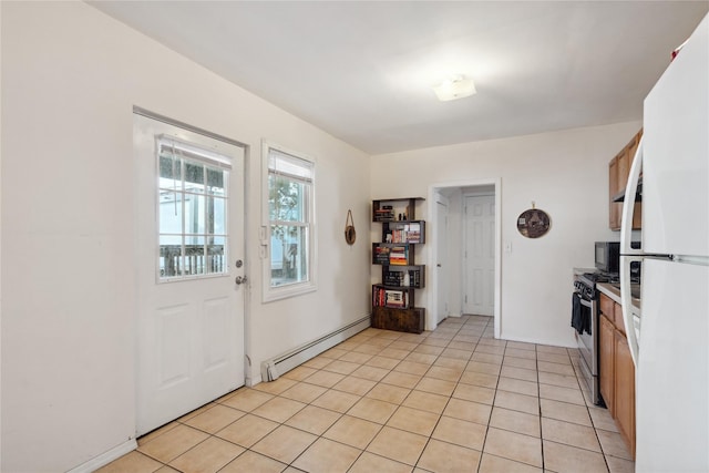 kitchen with light tile patterned floors, baseboard heating, stainless steel range with gas cooktop, and white fridge