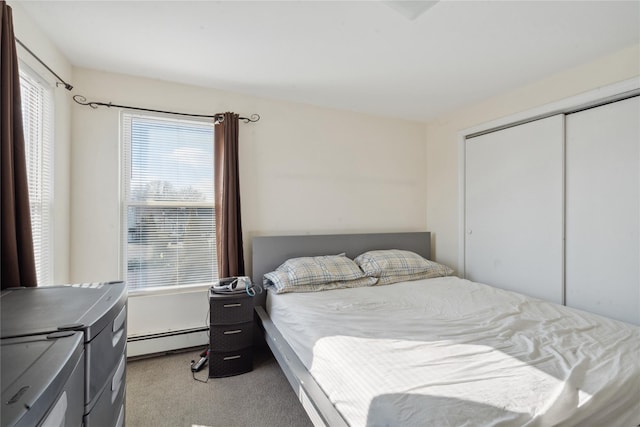 bedroom with light colored carpet, multiple windows, a baseboard heating unit, and a closet