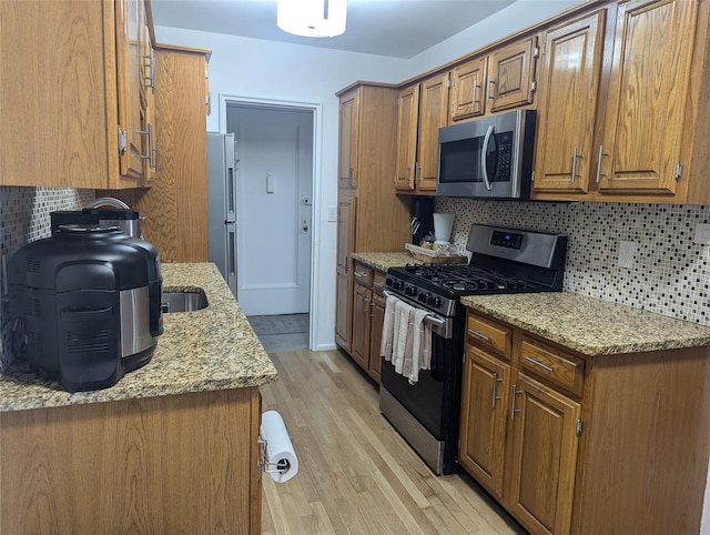 kitchen featuring tasteful backsplash, light stone countertops, light hardwood / wood-style floors, and appliances with stainless steel finishes