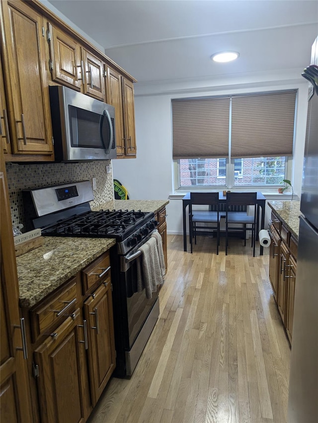 kitchen featuring backsplash, light wood-type flooring, light stone countertops, and appliances with stainless steel finishes