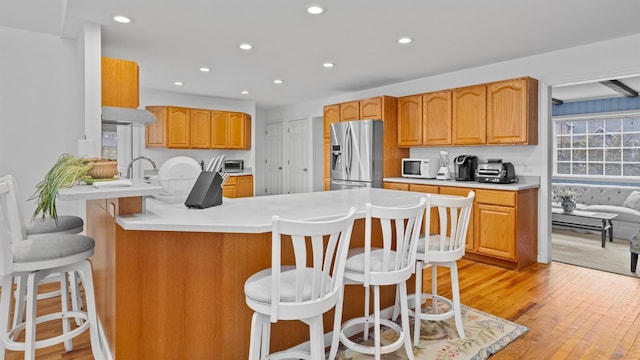 kitchen featuring kitchen peninsula, stainless steel fridge with ice dispenser, a breakfast bar, and light wood-type flooring