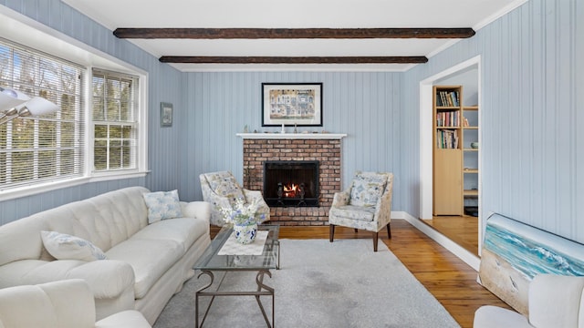 living room with beamed ceiling, hardwood / wood-style flooring, and a brick fireplace