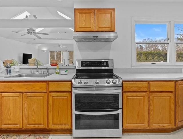 kitchen featuring brown cabinetry, light countertops, under cabinet range hood, double oven range, and a sink