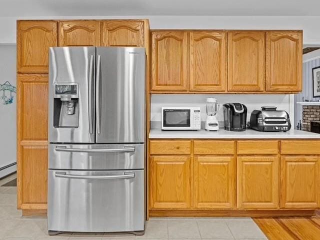 kitchen featuring light countertops, white microwave, stainless steel fridge, and brown cabinets