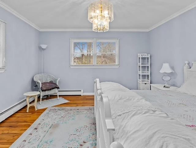 bedroom featuring a notable chandelier, crown molding, baseboard heating, wood finished floors, and baseboards