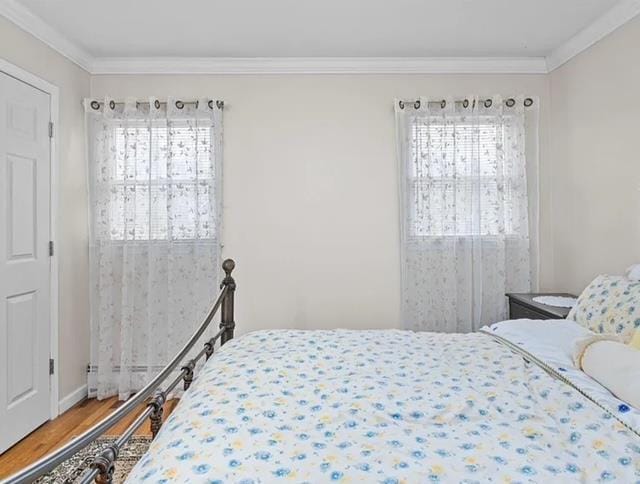 bedroom with multiple windows, crown molding, baseboards, and wood finished floors