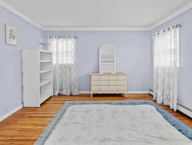 bedroom with multiple windows, wood finished floors, and baseboards