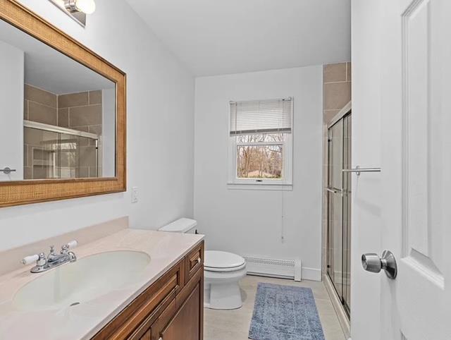 full bathroom with a stall shower, toilet, vanity, and baseboard heating