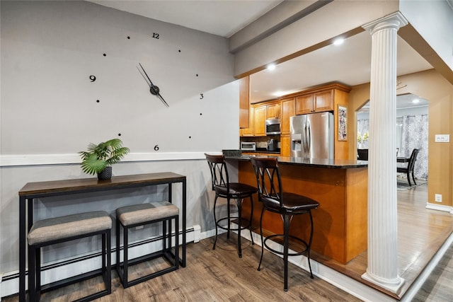 kitchen with kitchen peninsula, appliances with stainless steel finishes, light wood-type flooring, ornate columns, and a baseboard radiator