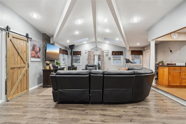 living room with lofted ceiling with beams, a barn door, and light hardwood / wood-style flooring