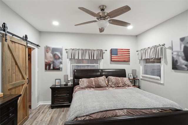 bedroom featuring a barn door, ceiling fan, and light wood-type flooring