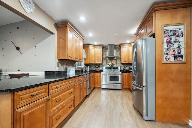 kitchen with stainless steel appliances, wall chimney range hood, light hardwood / wood-style flooring, backsplash, and dark stone counters