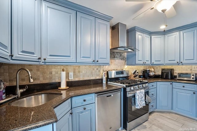 kitchen featuring wall chimney exhaust hood, stainless steel appliances, blue cabinets, sink, and dark stone countertops